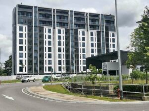 Eight-story modern apartment building with white and dark panels, glass balconies, along a curved road with greenery in front.