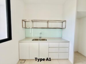 Compact kitchenette with white base cabinets, stainless sink, frosted glass backsplash, and a metal open shelf; window on the left.
