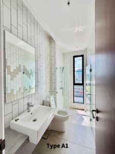 Bright modern bathroom with white subway tiles, a wall-mounted sink, toilet, and a glass-enclosed shower beside a tall window showing a city view.