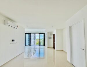 Bright empty living room with white walls, glossy tile floor, wall air conditioner, and large glass doors opening to a balcony with a city view.
