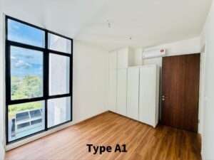 Modern empty bedroom with a large black-framed window, white walls, and built-in white wardrobes beside a wooden door.