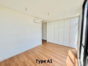 Vacant modern room with light wood flooring, white walls, a large built-in white wardrobe, and a window on the right letting in sunlight.