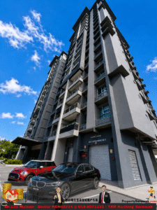 Tall modern condominium tower with balconies against a bright blue sky, with cars parked in front.