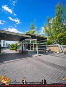 Guard booth at the gated entrance of a residential complex with a barrier arm and paved driveway under a bright blue sky