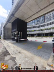 Underpass of a modern office complex with an elevated concrete roadway overhead, a barrier gate at the entrance, and a glass-front building in the background; banner ads at the bottom.