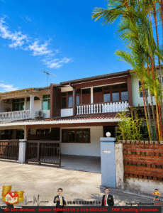 Two-story tropical-style house with a brown and white facade, gated driveway, and palm trees under a blue sky.