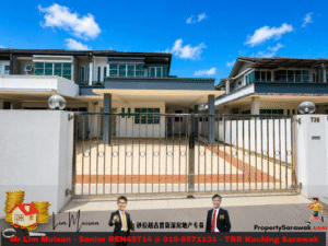 Front view of a two-story modern house behind a metal gate with a tiled driveway and a bright blue sky; a promotional banner with two men in suits and real estate text runs along the bottom.