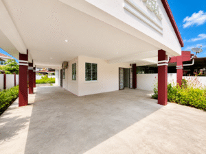 Covered carport area of a modern white house with maroon pillars and a concrete driveway under a bright blue sky.