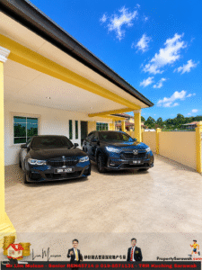 Two dark cars parked side by side under a yellow-framed carport on a residential driveway, blue sky overhead.