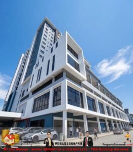 Angle view of a white modern multi-story building with large glass windows against a blue sky, with people and parked cars at the street level.