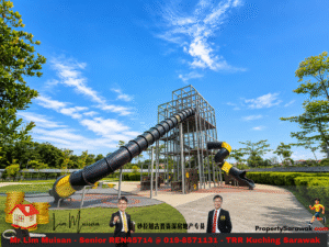 Bright blue sky over a modern outdoor playground with tall metal tower and black and yellow slides/tunnels under a lattice frame, surrounded by greenery.