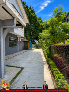 Concrete backyard path beside a gray house, with a blue storage shed, air conditioner, and lush trees along a chain-link fence under a bright blue sky of scattered clouds.