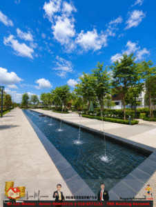 Long rectangular fountain pool with synchronized water jets on a paved park walkway under a bright blue sky.