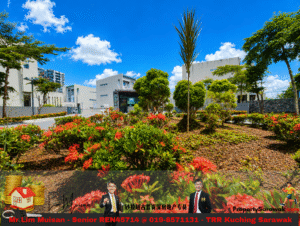 Modern campus-style buildings with manicured garden and red-flowering shrubs under a blue sky.