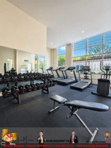 Well-lit gym interior with two rows of treadmills by large windows and a dumbbell rack in the foreground.