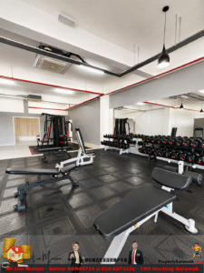 Bright, modern gym interior with weight benches, dumbbells on a rack, a large mirror along the wall, and assorted weight machines on a rubber-tiled floor.