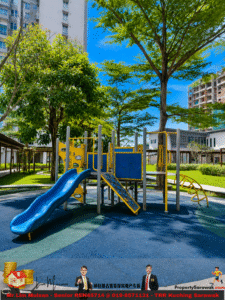 Playground equipment with blue slides and climbing structures in a sunny courtyard surrounded by trees and tall apartment buildings in the background.