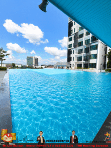 Large outdoor swimming pool beside a modern white apartment building under a blue canopy; bright blue sky with fluffy clouds above.