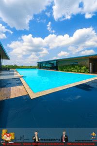 Outdoor modern swimming pool beside a glass-walled building under a blue sky with white clouds.