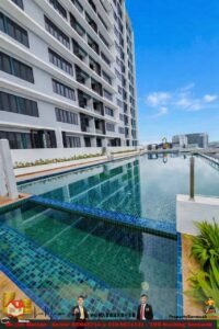 Rooftop swimming pool beside a modern white apartment building with a clear blue sky and city skyline in the distance.