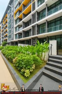 Exterior view of a modern multi-story residential building with yellow balconies and glass windows, beside a landscaped garden and steps to the entrance on the right