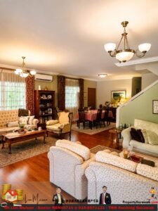 Spacious traditional living room with cream sofas, wooden coffee table, and a dining area in back, warm lighting from chandeliers.