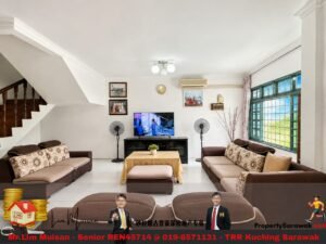 Living room with brown sectionals around a central coffee table, TV stand, ceiling light, two standing fans, and large green-framed windows on the right.