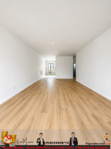 Empty open-plan living area with light wood flooring and white walls; kitchen at far end with window