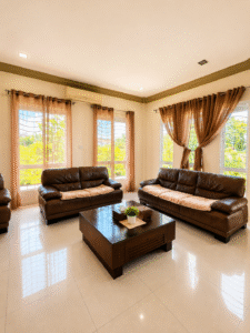 Living room with dark brown leather sofa set, a matching coffee table, and beige curtains letting in natural light.