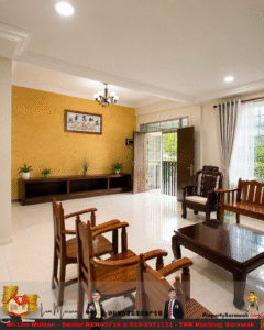 Spacious living room with wooden seating, yellow accent wall, and potted plants under a chandelier, open door to a gated exterior.