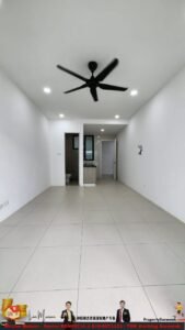 Empty, bright, rectangular room with large beige tile floor, white walls, and a black ceiling fan; kitchenette and doorway visible at the far end.