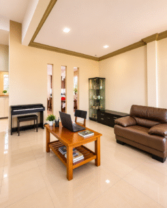 Spacious modern living room with beige walls, brown leather sofa, wooden coffee table with a laptop, and a glass display cabinet.