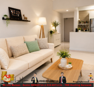 Bright, modern living room with a cream sofa, green and patterned pillows, wooden coffee table, and a tall floor lamp, open to a white kitchen with a bar area and plants on display.