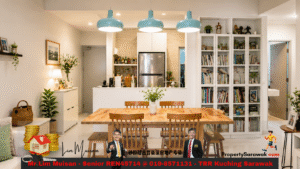 Bright open-plan kitchen and dining area with a wooden table, six chairs, white cabinetry, and a bookshelf-filled wall on the right; teal pendant lights above the table.