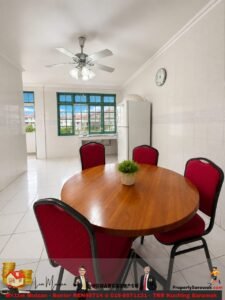 Bright dining area with a round wooden table, four red chairs, and white-tiled kitchen walls under a ceiling fan.