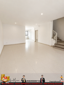 Bright empty open-plan living area with white walls, tiled floor, a staircase on the right, and a doorway to a back room/kitchen area in the distance.