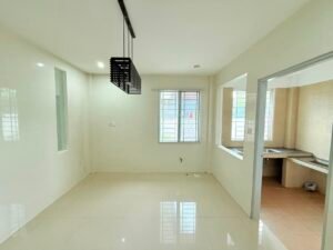 Bright, empty kitchen/dining space with white tiled floors and walls, a black rectangular pendant light, a window, and a doorway to a separate kitchen with a sink visible through a pass-through opening.