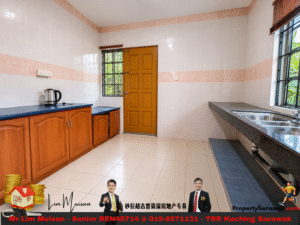 Bright kitchen with beige tiled walls, brown wooden cabinets along the left, blue countertops, a kettle on the counter, a brown door, a window to the outside, and a double stainless steel sink on the right.