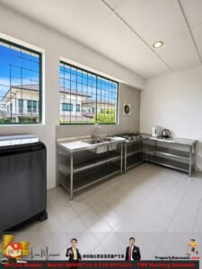 Bright, empty commercial kitchen with stainless steel countertops, a double sink, gas stove, and small appliances on the right; large windows with grid bars provide a view of neighboring houses outside. White walls and tiled floor create a clean, modern space.