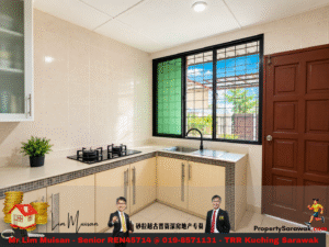 Compact L-shaped kitchen with beige tiled walls, gas stove, and a double sink under a large window with green pane accents and a wooden door to the right
