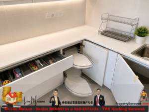 Modern white kitchen with an open lower corner cabinet revealing a curved pull-out shelf and utensil drawer contents (scissors, utensils, etc.).