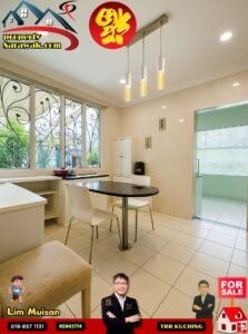 Bright, modern kitchen with a black round dining table and white chairs, illuminated by three pendant lights; large decorative windows to the left and a glass door to a pale room on the right. Overlaid logos show a property listing and a 'FOR SALE' badge at the bottom.