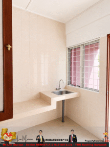 Beige-tiled kitchenette with a small counter and stainless steel sink, barred window to the right, wooden door frame on the left.