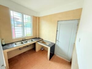 Compact kitchen with beige tile walls, a double stainless steel sink under a window, and a gray door.