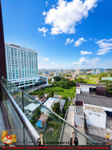 Wide city view from a balcony: glass railing, the Pullman hotel on the left, skyline and blue sky with clouds.