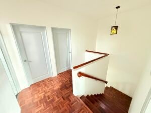 Stairwell at a landing with wooden handrails and two closed light-gray doors on the left wall.