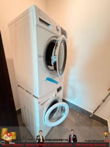 Stacked white front-loading washing machine and dryer in a small laundry alcove with tiled floor and a mop handle on the wall to the right.