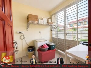 Small utility balcony with a washing machine, storage bins, and metal shelf against a pale wall. Large louvered windows let in daylight.