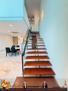 Modern open-concept interior with a floating wooden staircase along a pale blue wall, glass railing, and marble floor; a dining table with dark chairs is to the left.