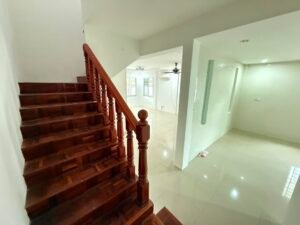 Interior of a bright, empty living space with a wooden staircase on the left and glossy tiled floors.